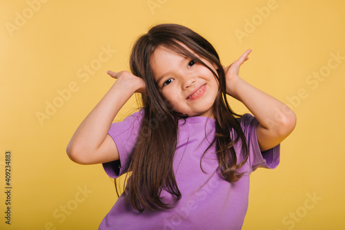 beautiful little girl in a purple t-shirt posing on a yellow background. Cute baby makes faces.