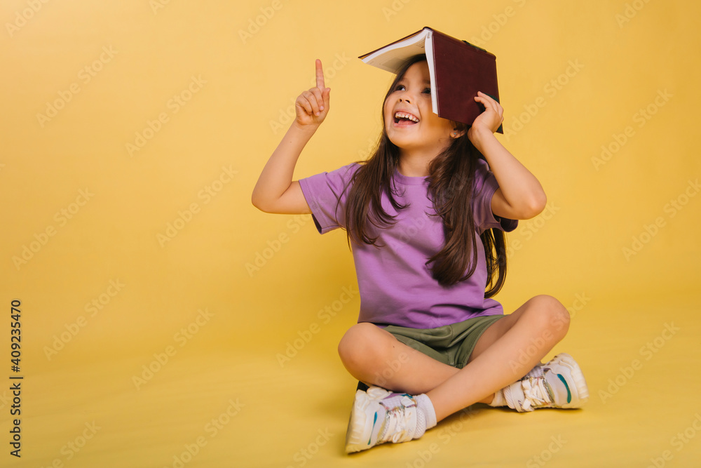 beautiful little girl holding a book on her head while sitting, playing ...