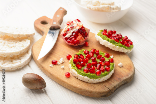 Rice cakes with avocado mash and pomegranate seeds on cutting board