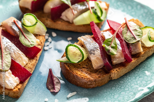 Sandwich with pieces of marinated herring fillet, beetroot salad, green cucumber, onion and microgreen. Toast with herring fillet. Scandinavian cuisine