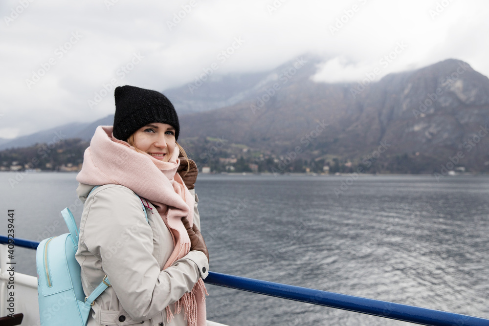 Passage cruise woman tourist in fjords Scandinavian countries. Dressed in hat, scarf and backpack. Looks into distance mountains in fog Passage cruise woman tourist in fjords Scandinavian countries. Dressed in hat, scarf and backpack. Looks into distance mountains in fog