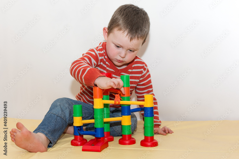 The child sits and launches a small ball into the maze, through which he rolls. The boy is focused, keen on the game. Educational games for children. Horizontal photo. The child sits and launches a small ball into the maze, through which he rolls. The boy is focused, keen on the game. Educational games for children. Horizontal photo.