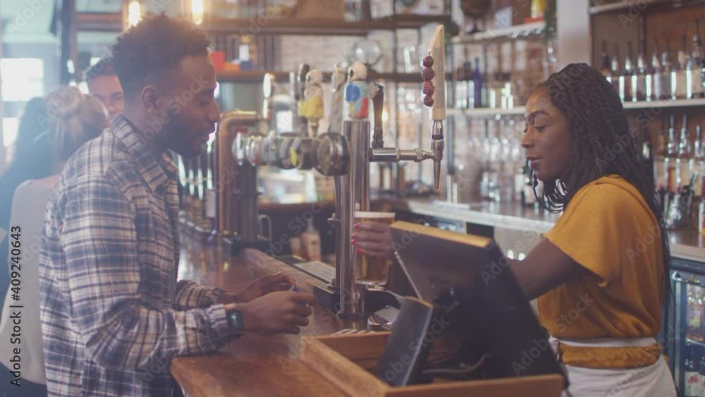 Male customer in bar paying bartender for drink using contactless card and social distancing during health pandemic - shot in slow motion Male customer in bar paying bartender for drink using contactless card and social distancing during health pandemic - shot in slow motion