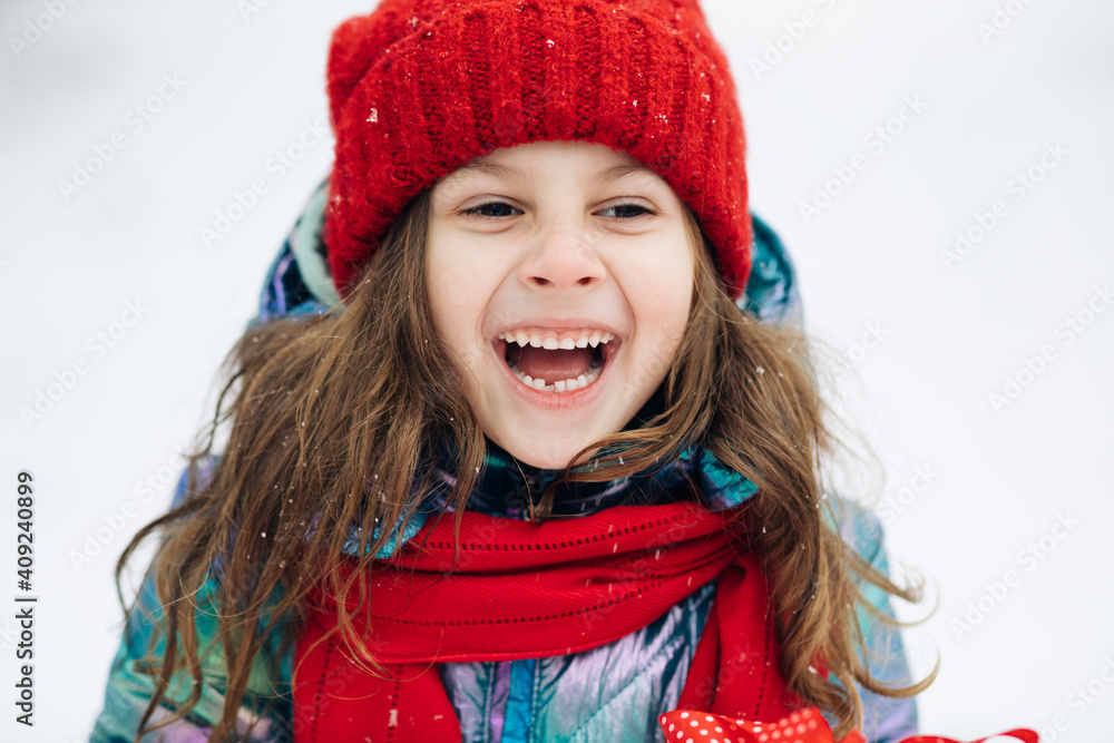 Close up of the happy cute girl looking at the camera and smiling the background of a snowy forest. Positive child. Portrait shot. Outside. The dead of winter, cold weather, frost, snow Close up of the happy cute girl looking at the camera and smiling the background of a snowy forest. Positive child. Portrait shot. Outside. The dead of winter, cold weather, frost, snow