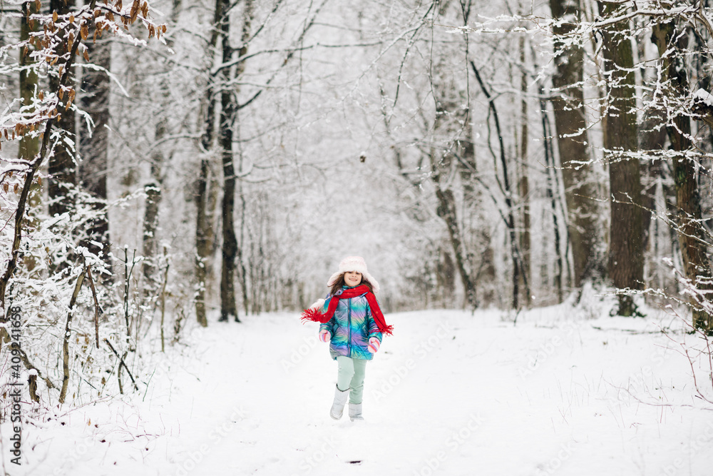 Happy child girl plays with a snow in winter day. Girl enjoys winter, frosty day. Cute little happy girl in winter clothes is having fun running in snowy winter day