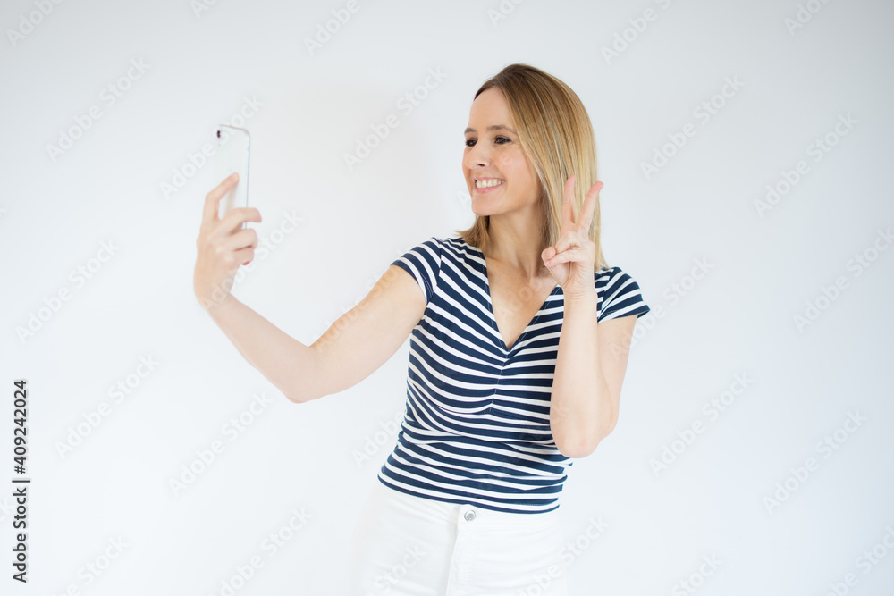 Portrait of a smiling happy woman showing victory sign and looking at mobile phone isolated over white background Portrait of a smiling happy woman showing victory sign and looking at mobile phone isolated over white background