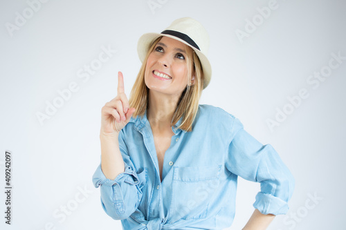 Portrait of a happy young woman dressed in denim shirt pointing finger up at copy space isolated over white background © Danko