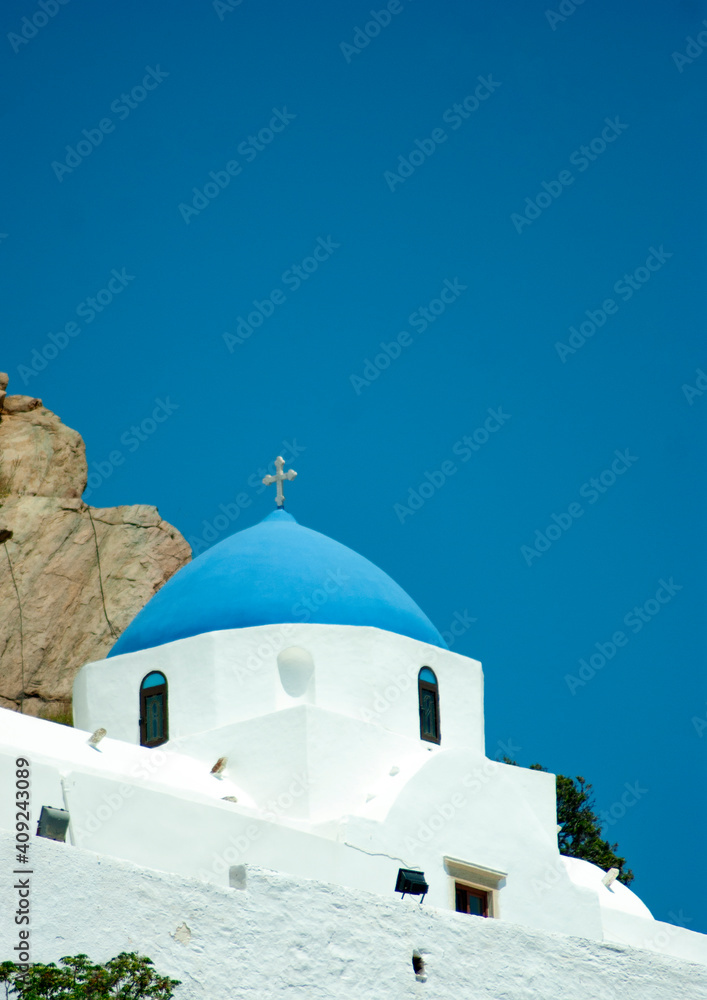Ios, Greece. Beautiful traditional chapel on hillside above the islands old village. Vertical view with clear blue sky for copy space. Detailed shot of old church and light blue dome. Ios, Greece. Beautiful traditional chapel on hillside above the islands old village. Vertical view with clear blue sky for copy space. Detailed shot of old church and light blue dome.