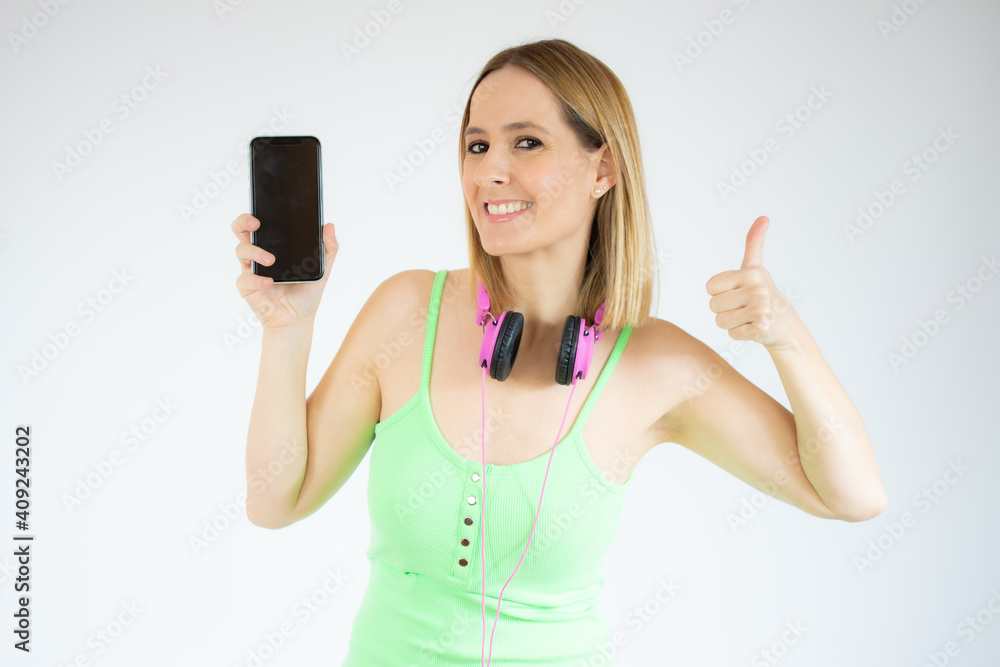 Young happy cheerful woman in headphones showing mobile phone with thumb up over white background. Young happy cheerful woman in headphones showing mobile phone with thumb up over white background.
