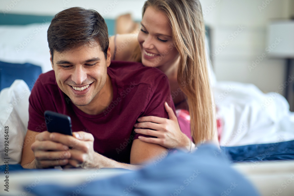 Young couple in love enjoying smartphone content together in the bed at the hotel room. Couple, love, hotel, together - obrazy, fototapety, plakaty 