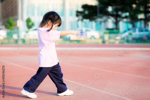 Side view of Asian cute girl's is stretching her arms in front of her to act like a zombie or ghost. Child have fun in the sports field. Happy children. A good-natured kid wearing pink shirt, ages 3-4