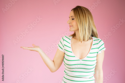 Young beautiful woman showing something or copy space for product or sign text, isolated over pink background