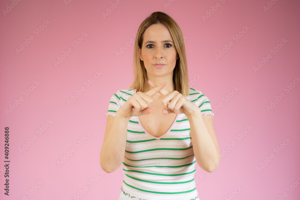Young woman wearing striped t-shirt standing over pink isolated background Rejection expression crossing fingers doing negative sign Young woman wearing striped t-shirt standing over pink isolated background Rejection expression crossing fingers doing negative sign