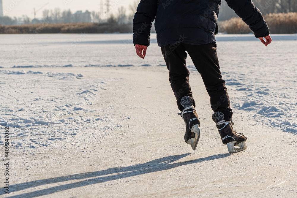 Skater legs at skating rink. Man skating on white ice on frozen lake. Back view. Winter leisure activity.