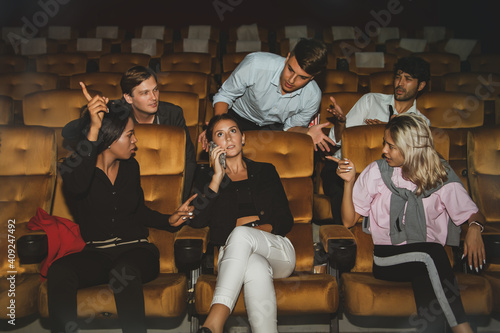 Young woman talking on the phone among moviegoers so annoying others that men and others who sit next to each other admonish her because she is not happy with her manners. photo