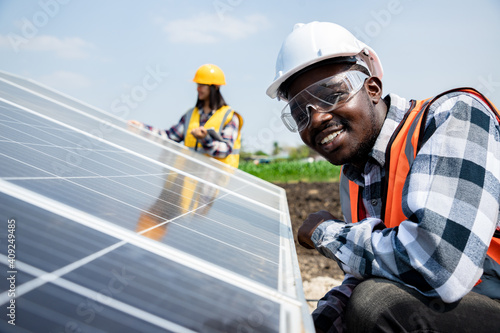 Two workers technicians installing heavy solar photo voltaic panels to high steel platform in corn field. Photovoltaic module idea for clean energy. Green energy concept