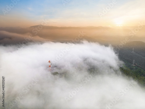 Aerial view, Beautiful Panorama landscape sunrise over peak Mountain with mist and warm light sunrise at signal repeater station pole, Communication technology concept. Mae Moh Lampang, Thailand