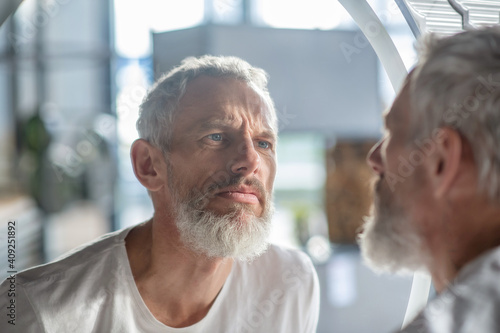 Φωτογραφία Bearded grey-haired man looking at the mirror