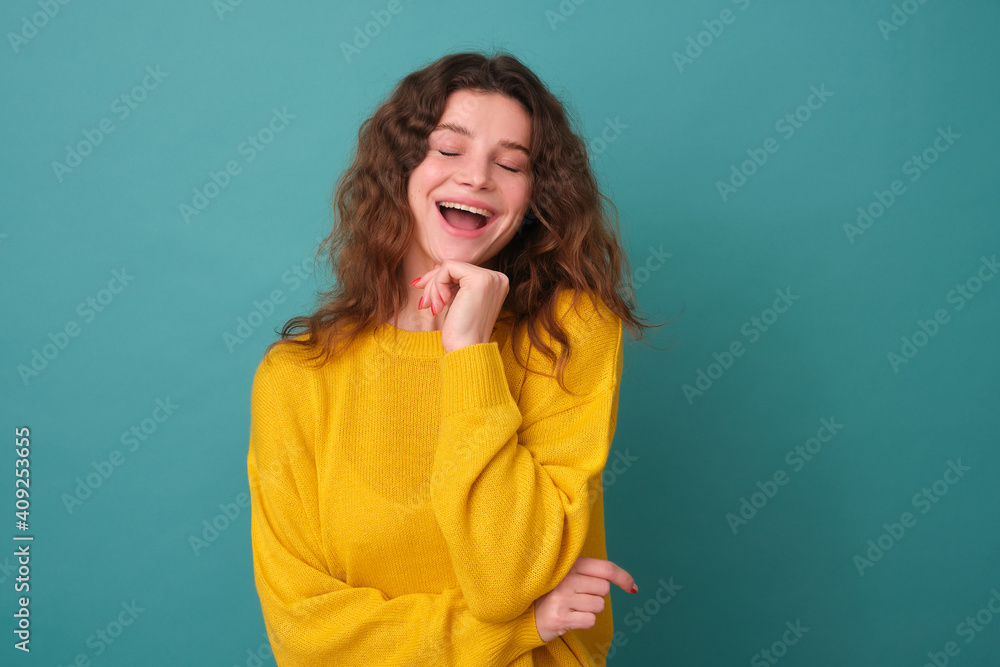 Cheerful beauty sincerely laughs, she has a shy expression, has an interesting idea, holds her hand on a hoodie, enjoys life, poses indoors on a blue background of the studio Cheerful beauty sincerely laughs, she has a shy expression, has an interesting idea, holds her hand on a hoodie, enjoys life, poses indoors on a blue background of the studio