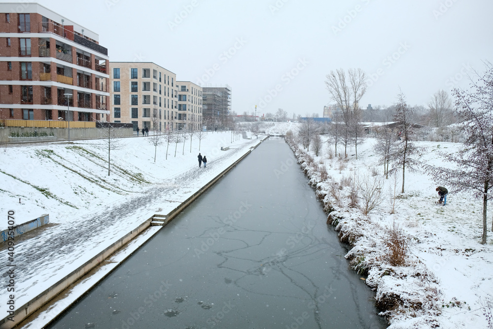 The snow-covered harbour in Leipzig's Neulindenau district in winter with icy paths and river.