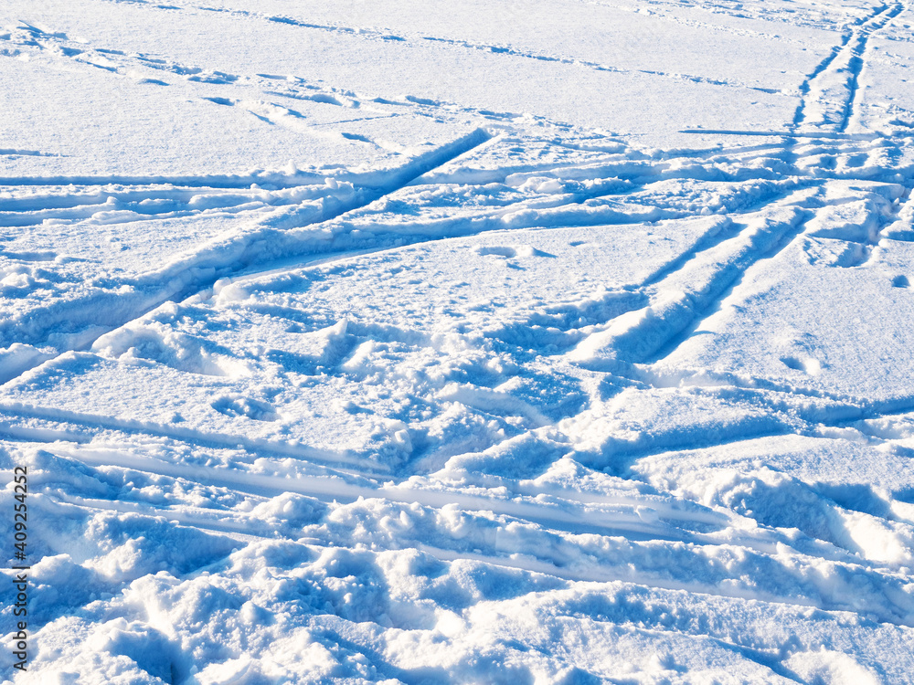 Obraz premium blue surface of snow with ski tracks and footprints lit by setting sun in cold winter twiligh
