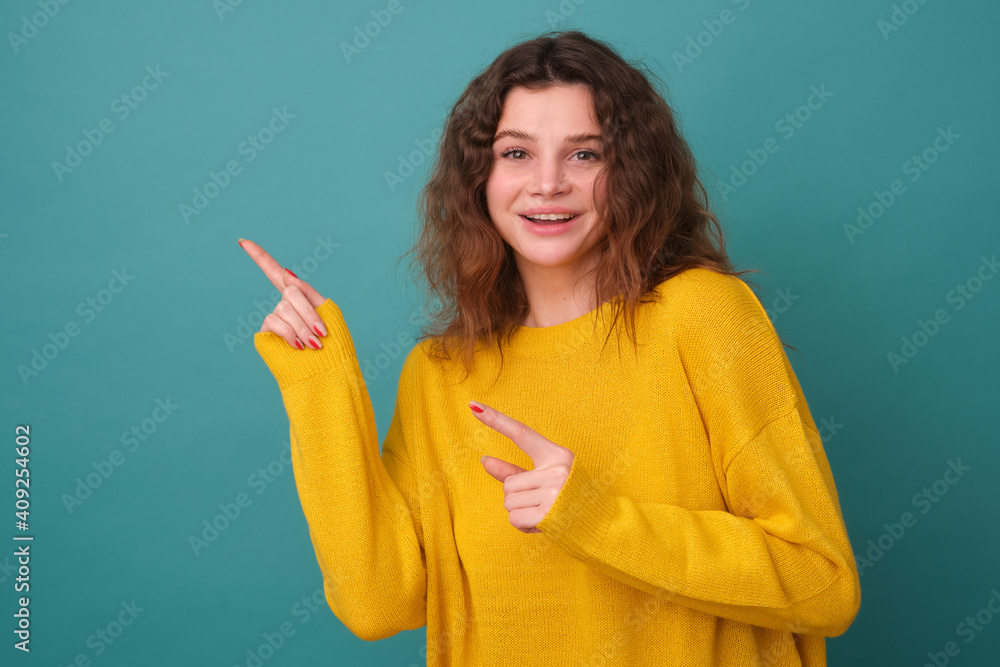 Cheerful girl with points to copyspace, shows a recommendation, suggests going in this direction or promo, wears a yellow sweater isolated on a blue background, makes a good choice Cheerful girl with points to copyspace, shows a recommendation, suggests going in this direction or promo, wears a yellow sweater isolated on a blue background, makes a good choice