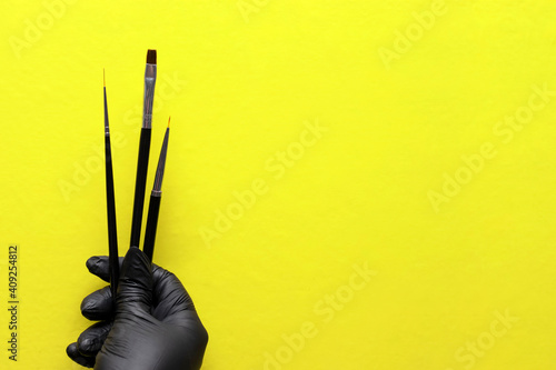 brushes for coating gel varnish in hand with a black glove and on a bright modern yellow background