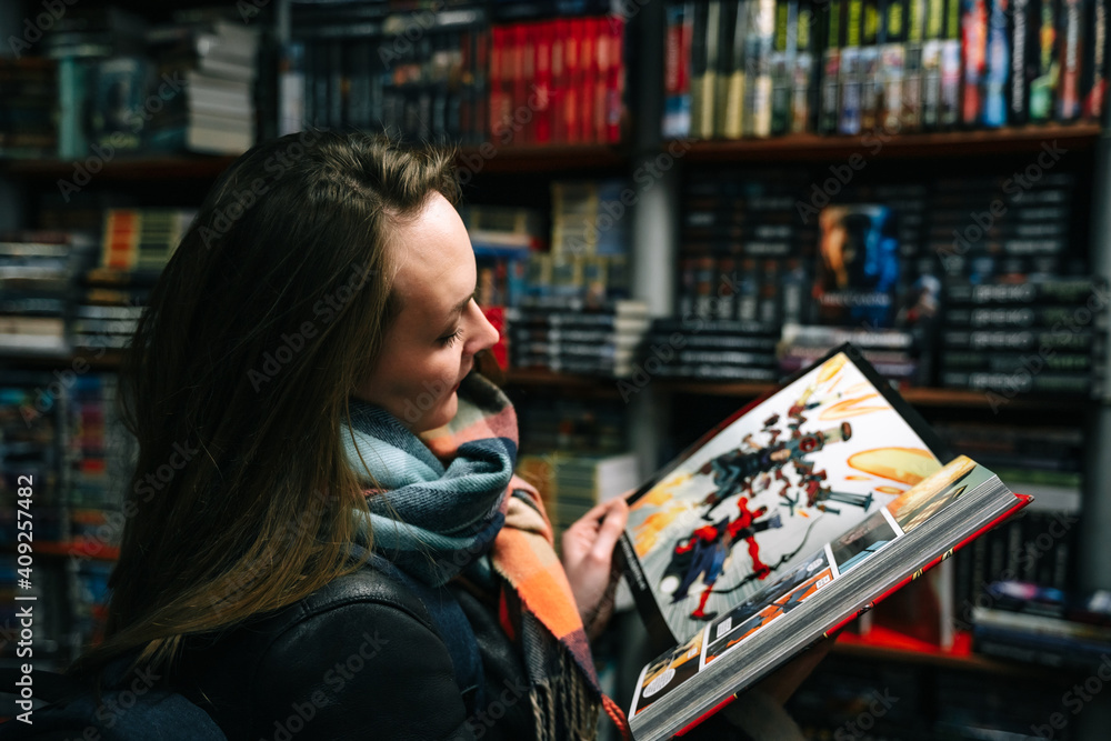 © marozzau - A beautiful woman in a book store holds an open comic book in the ruffs (the book is blurred).