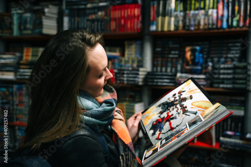 A beautiful woman in a book store holds an open comic book in the ruffs (the book is blurred).