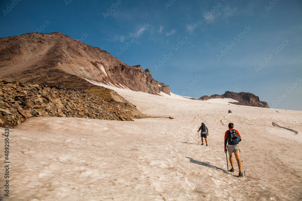 Two hikers climb towards the summit of Glacier Peak at dawn. Two hikers climb towards the summit of Glacier Peak at dawn.