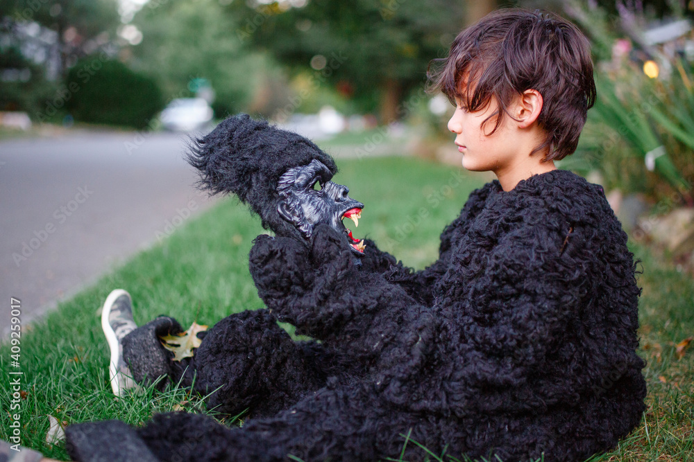 A boy sits in grass in gorilla suit looking at scary gorilla mask A boy sits in grass in gorilla suit looking at scary gorilla mask
