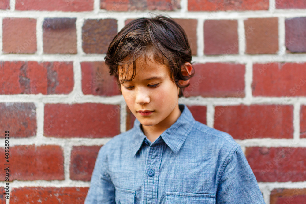 portrait of a young boy leaning against brick wall shyly looking down portrait of a young boy leaning against brick wall shyly looking down