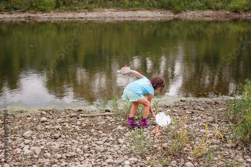 A little girl cleans litter up off of the shoreline of a river photo