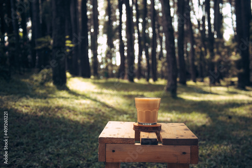 A cup of coffee on wooden table with outdoors green summer forest background 