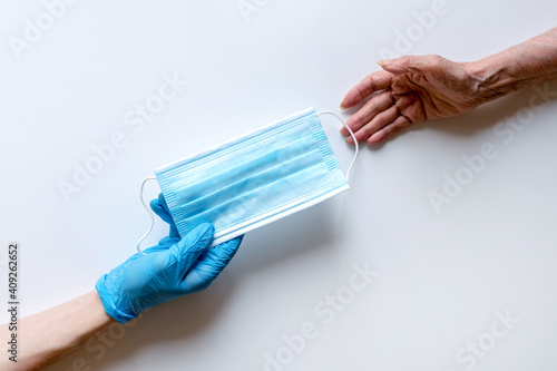 The doctor's hands in medical gloves on a white background pass the mask to an elderly woman.