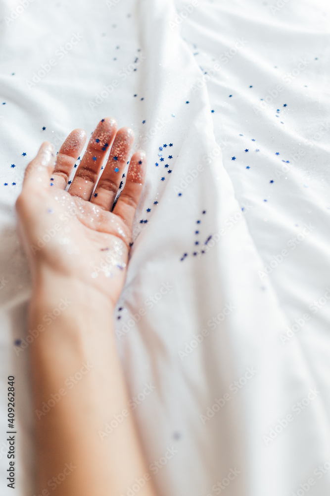 Women hand with blue stars and glitter confetti on white blanket Women hand with blue stars and glitter confetti on white blanket