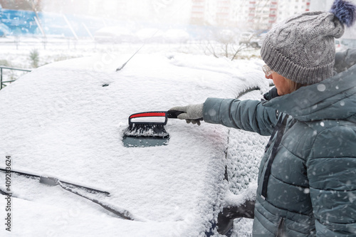 Woman cleans snow from the windshield of a car outdoors on a winter day