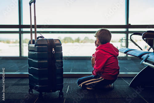 Young boy next to suitcase looking out the window at airport. photo