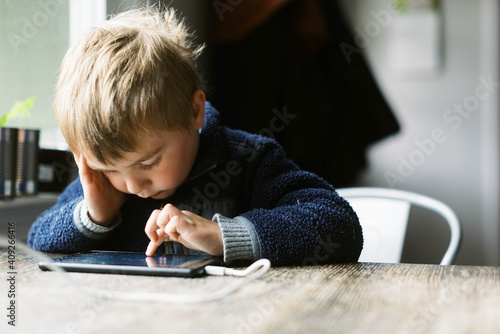 Little independent boy using his tablet for remote school at a table