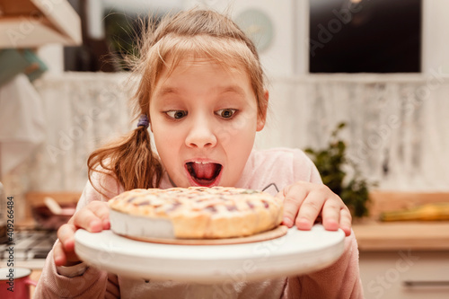 Little blonde girl bites an apple pie. The child wants to bite the cake