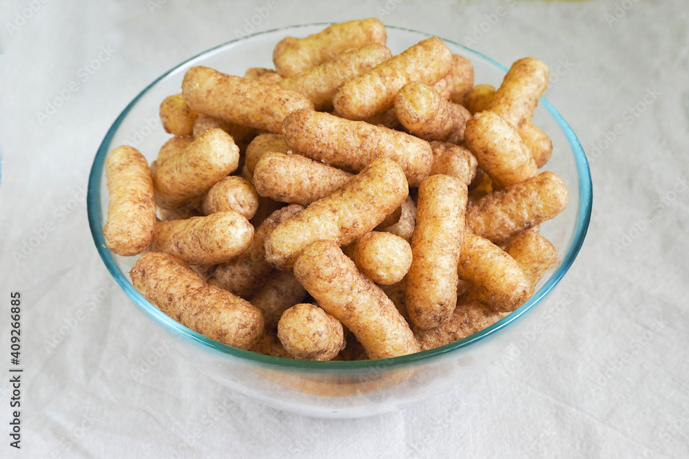 glass bowl with gluten-free corn sticks with cocoa on a beige tablecloth side view . sweet snacks for breakfast for children glass bowl with gluten-free corn sticks with cocoa on a beige tablecloth side view . sweet snacks for breakfast for children