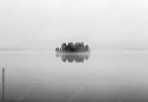 Lone island reflected in calm water of lake on foggy day, Maine