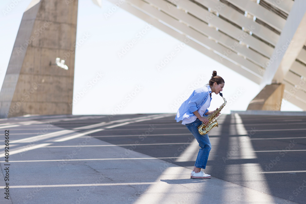 Woman with ponytail playing a saxophone while standing outdoors Woman with ponytail playing a saxophone while standing outdoors