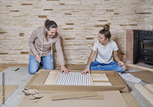 Front view of two women getting a piece of wood or shelf from a photo