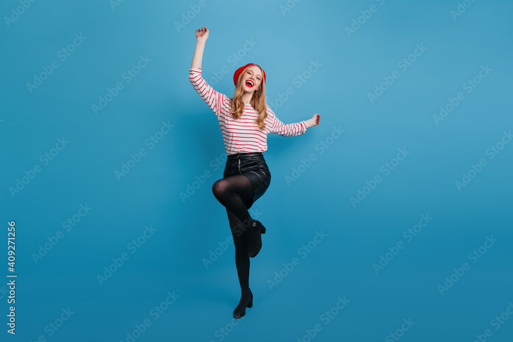 Excited stylish girl dancing on blue background. Full length view of pleasant blonde lady in black skirt.