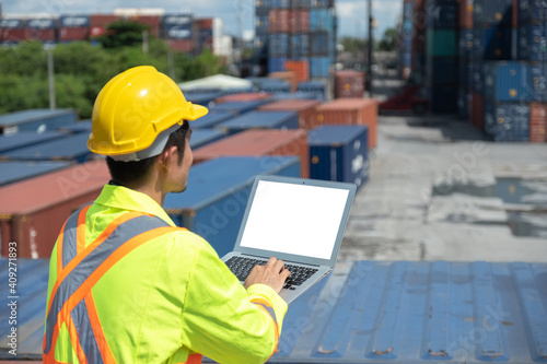 back view shipping worker or engineer using blank screen laptop in shipyard factory with containers and sky background with screen clipping path