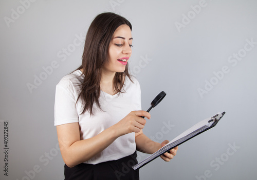 Businesswoman examines documents with a magnifying glass. Gray background.