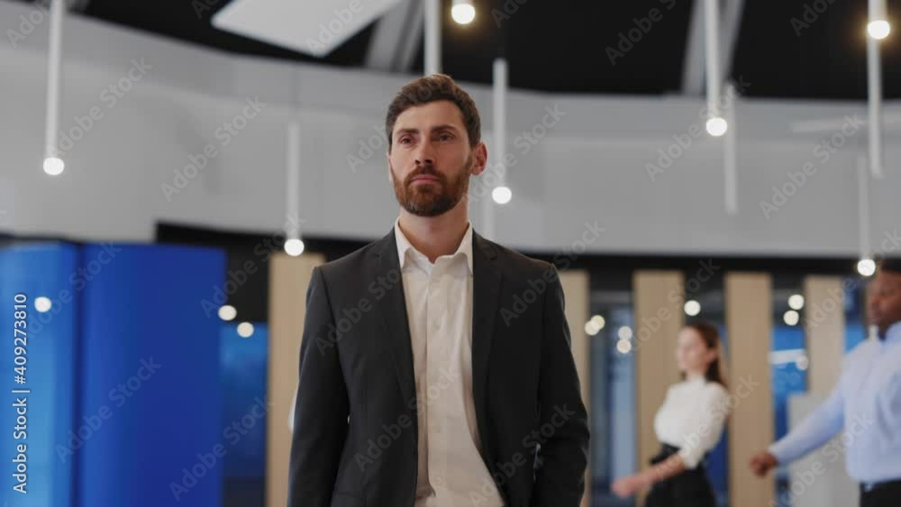 Young handsome entrepreneur walking confident along business center modern hall with corporate people on background. Successful person. Young handsome entrepreneur walking confident along business center modern hall with corporate people on background. Successful person.