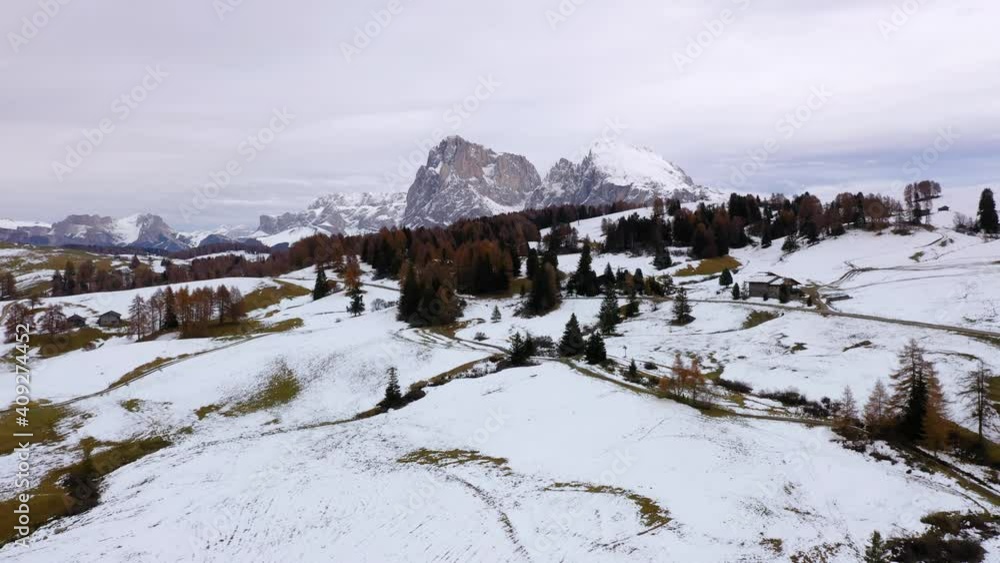 Backwards aerial shot of mountains and snowy alpine meadow at Seiser Alm - Alpe di Siusi plateau in the Dolomites, Italy