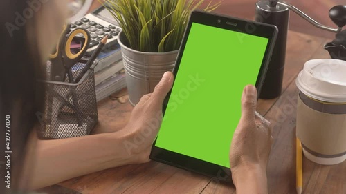 Over the shoulder shot of use digital tablet with green screen. Office desk background. Chroma key. Tablet with green screen in table